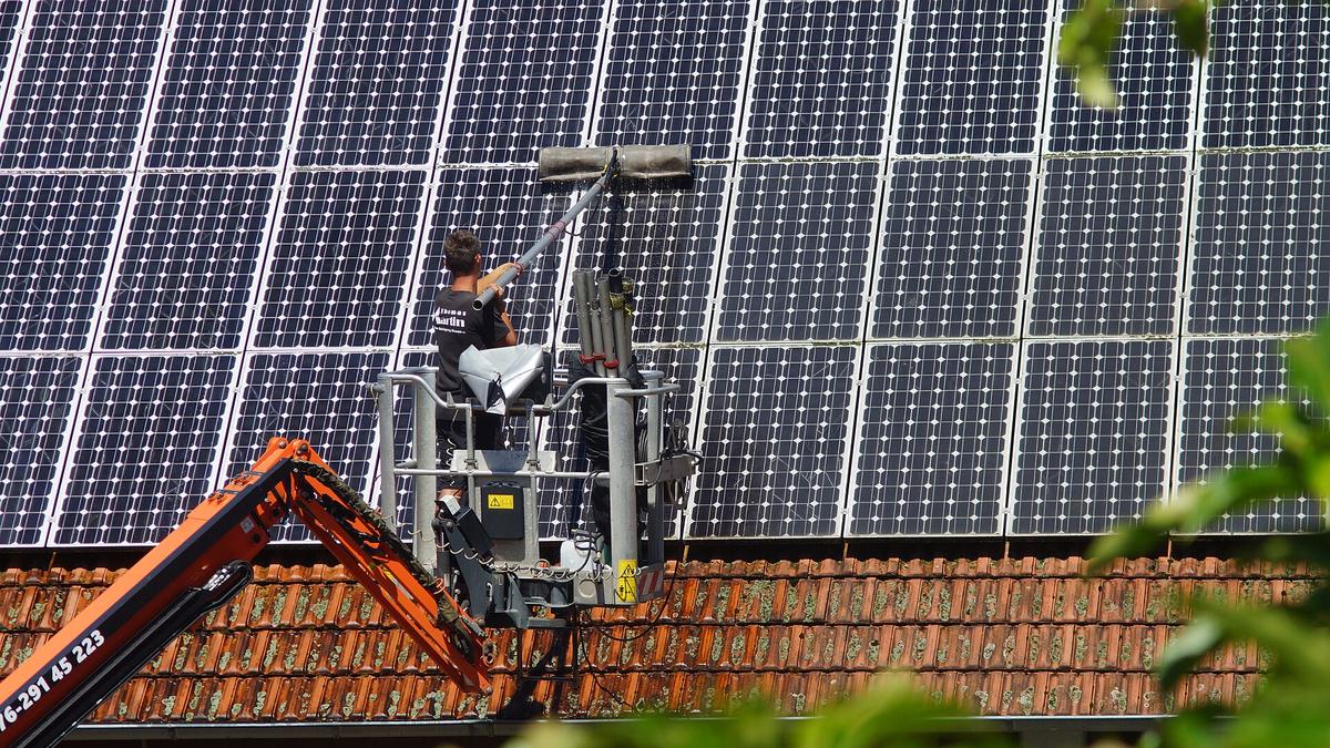 Schoonmaker reinigt vanuit een hoogwerker met een lange borstel de zonnepanelen op een oranje pannendak