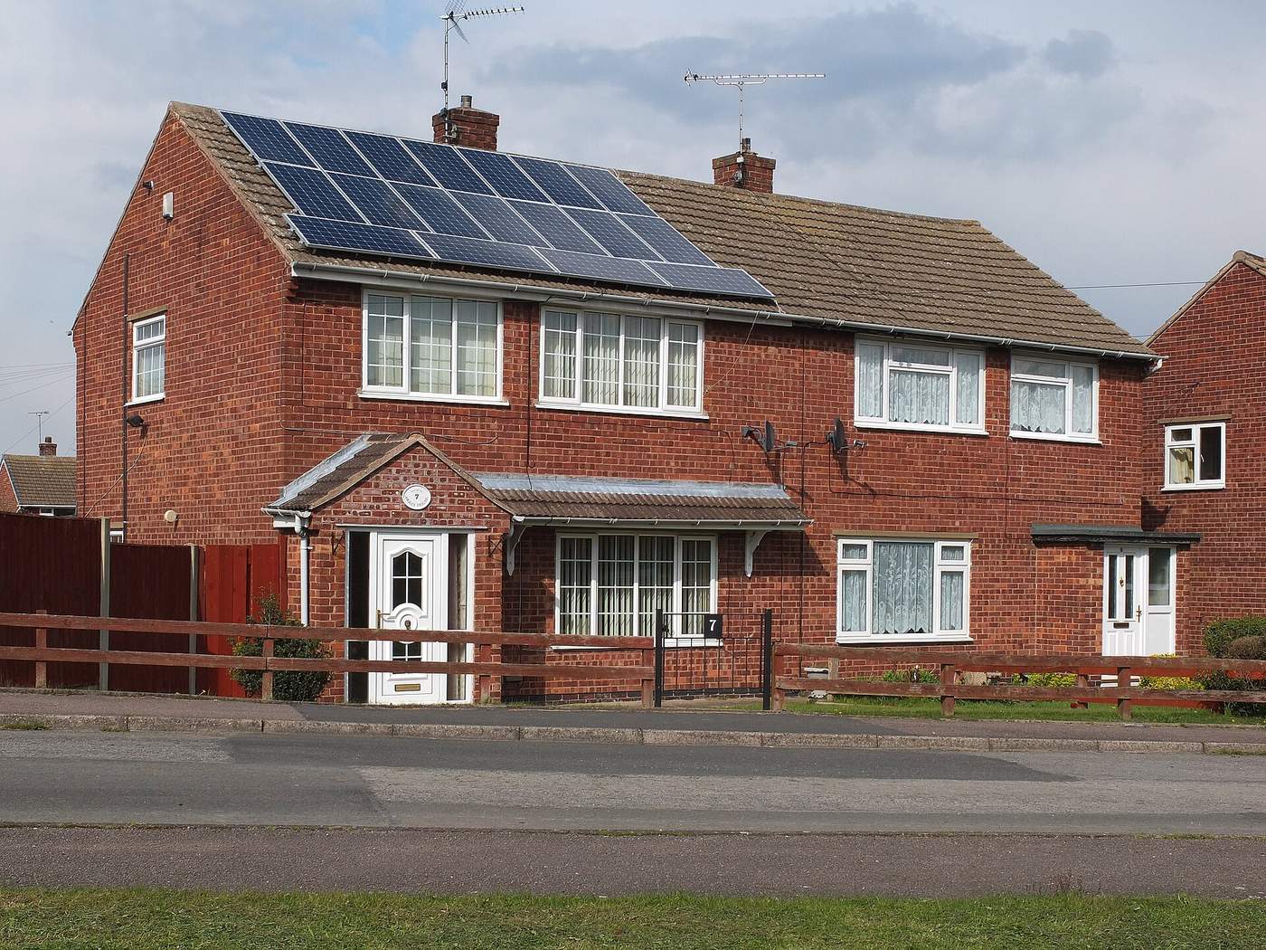 Halfopen woning in rode baksteen met een reeks zonnepanelen op het pannendak en een houten tuinhek vooraan