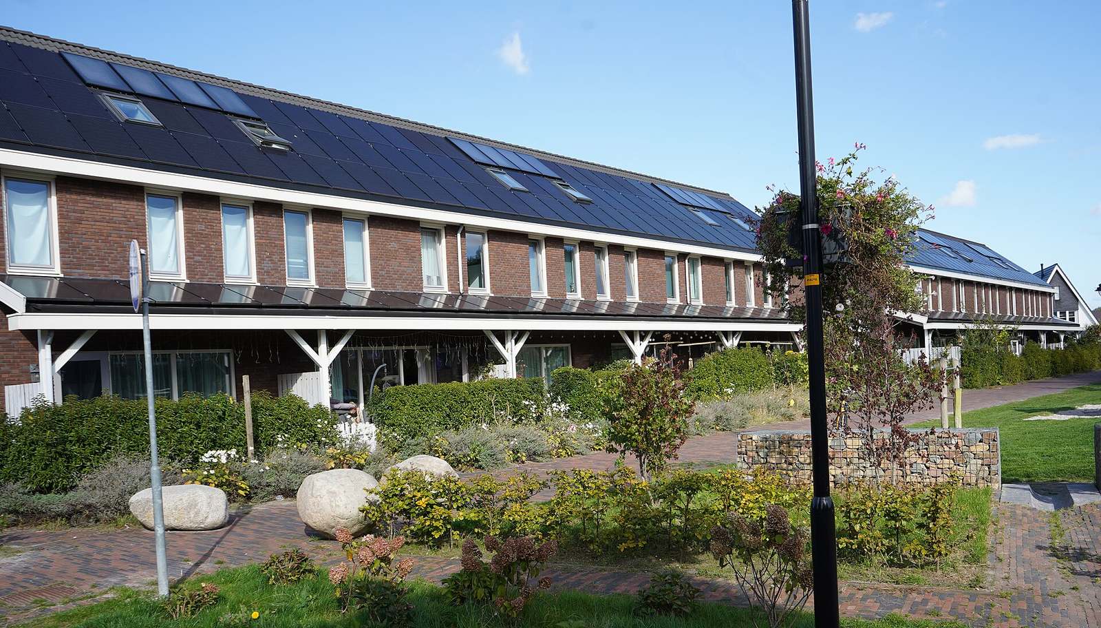 Rij woningen in rode baksteen met zwarte zonnepanelen en dakvensters over het hele dak, achter een groene voortuin